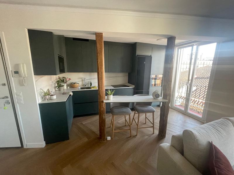 Cocina abierta en verde oscuro con barra entre pilares de madera