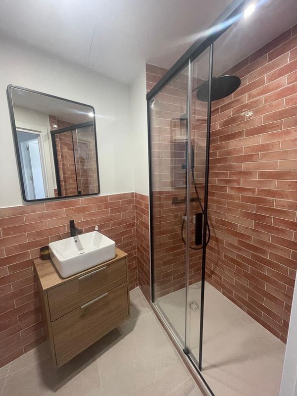 Baño con mampara negra y alicatado tipo ladrillo en salmón